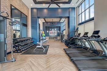 A gym with cardio machines and weights and windows